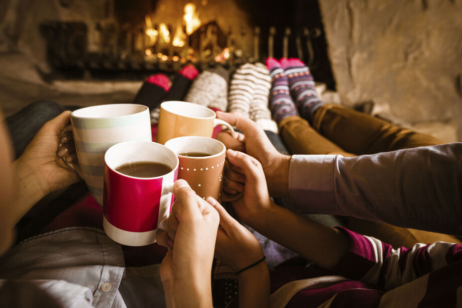 People sat in front of a fireplace with mugs of tea/coffee